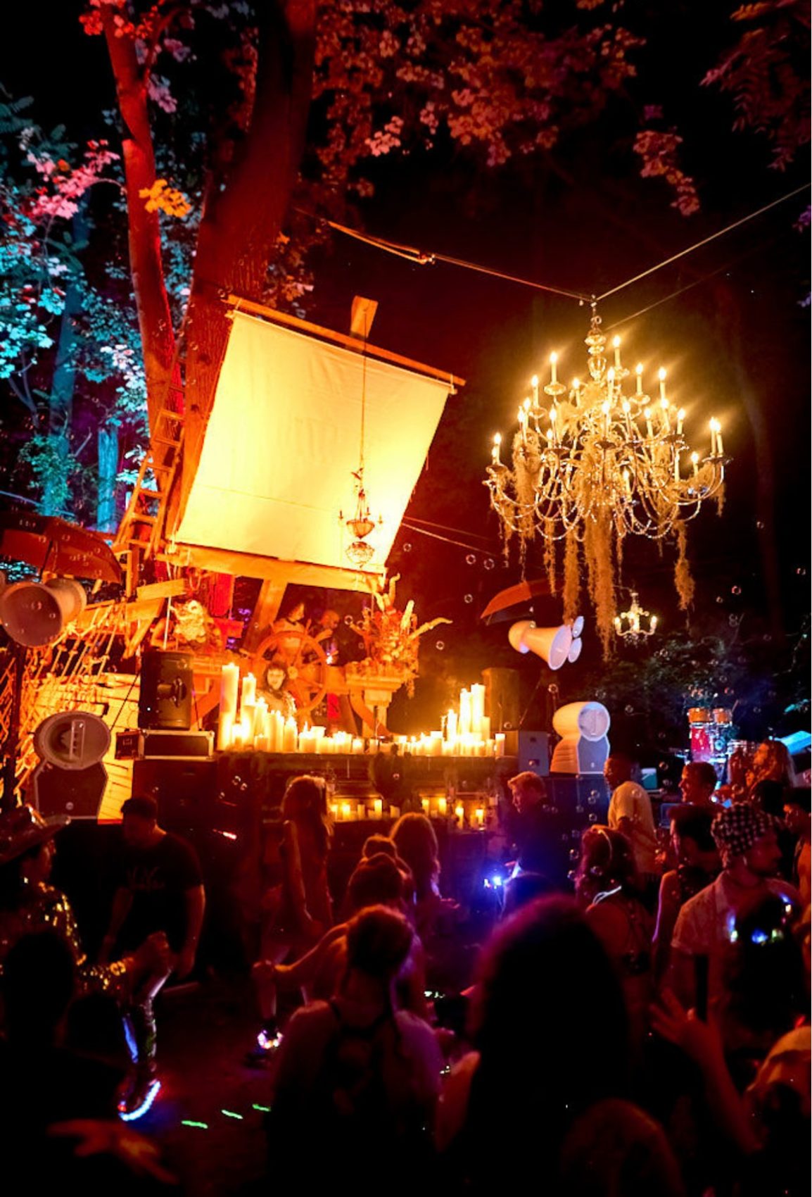 Chandeliers and a glowing sail over a forest dancefloor at night