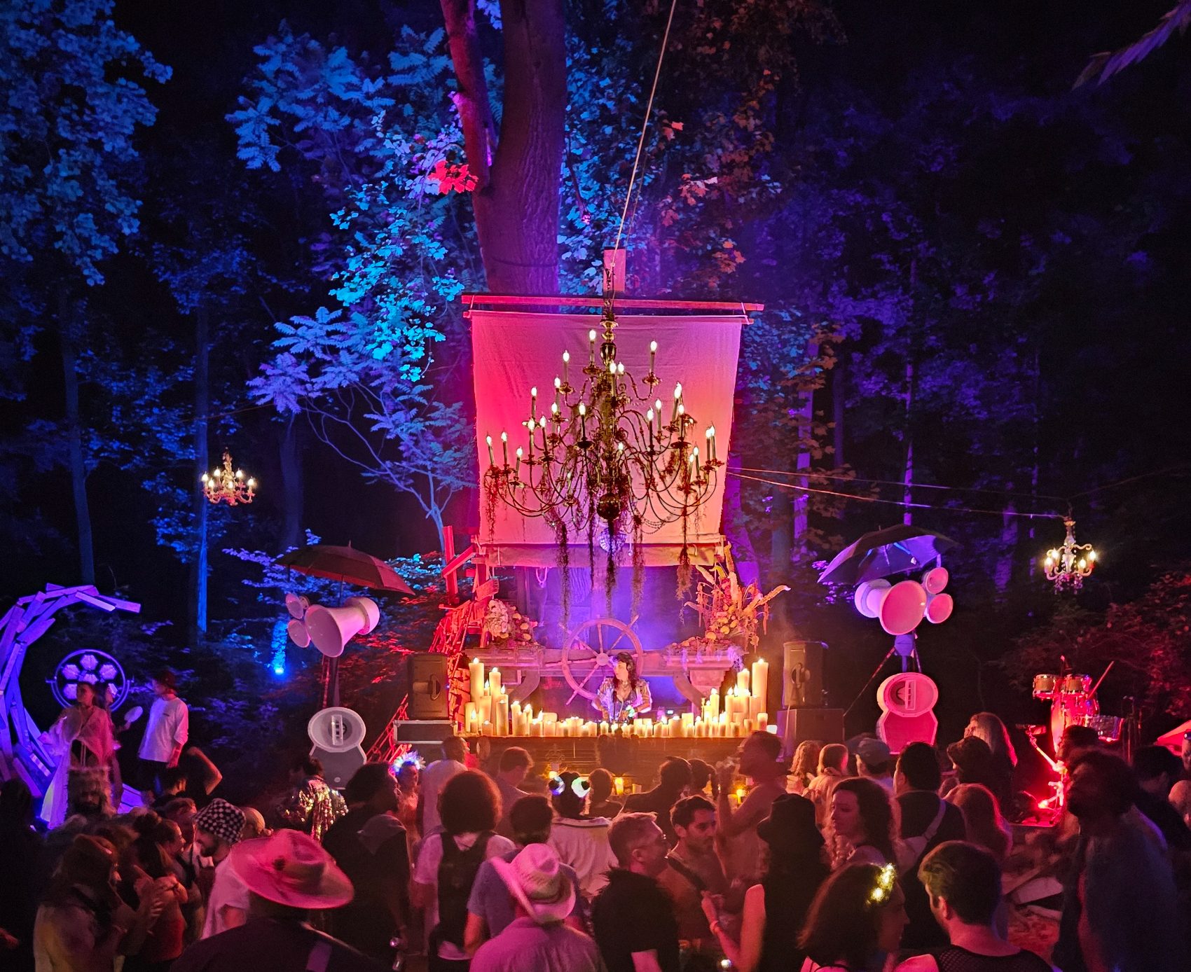 A packed dancefloor at a forest stage lit pink and blue, with Void horns on both sides