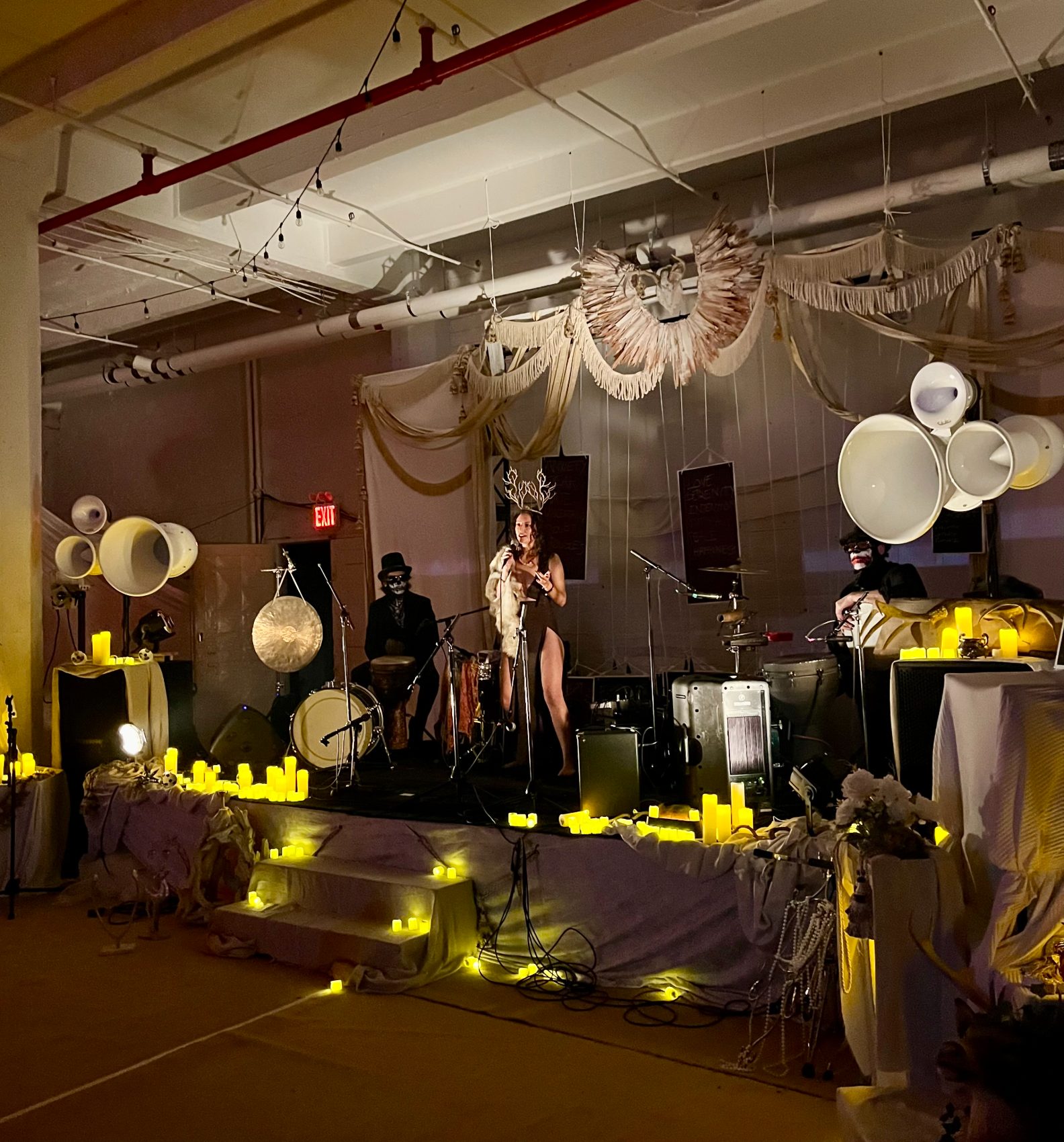 Performers on a candlelit loft stage draped in fabric, with white Void horn clusters on both sides