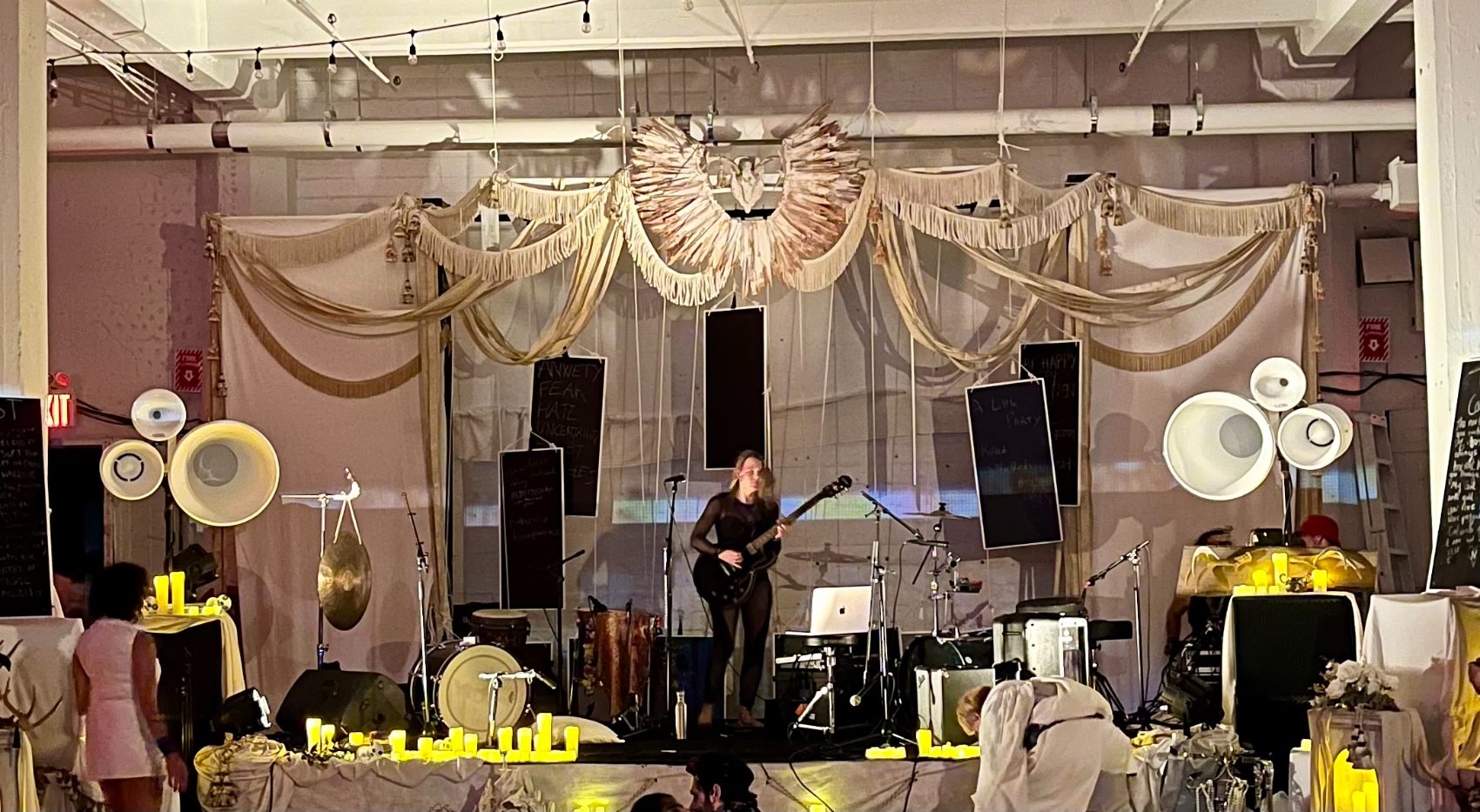 A guitarist on a fabric-draped loft stage in daylight, flanked by Void horn clusters