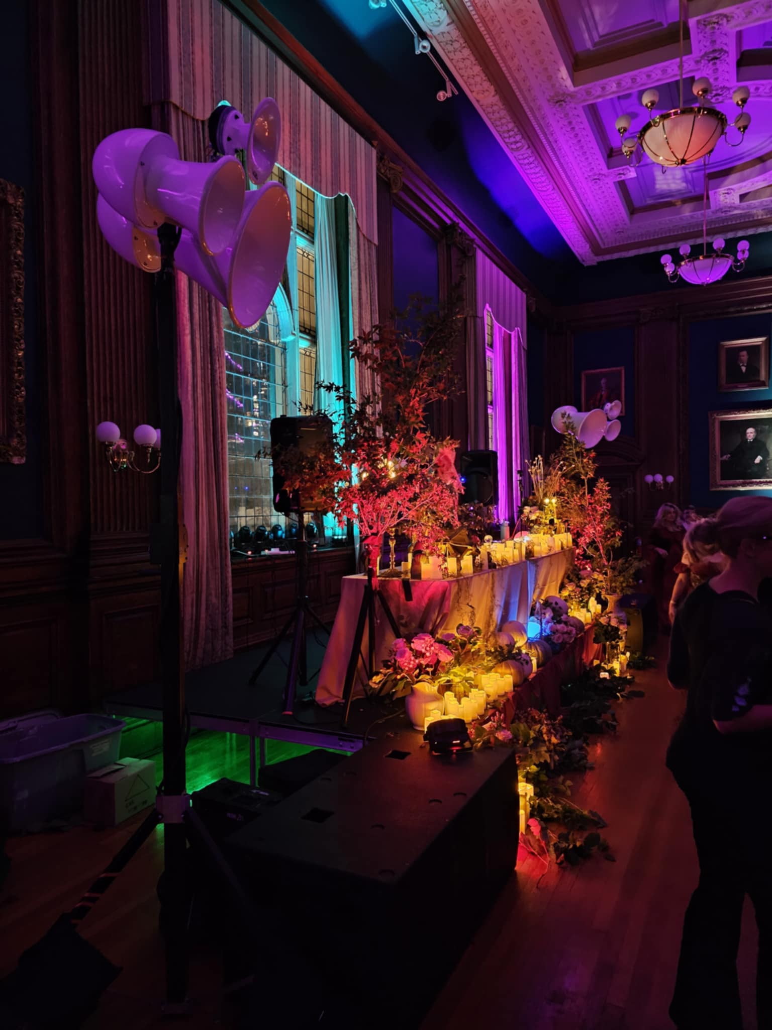A cluster of white Void horns on a stand in a wood-panelled ballroom lit purple, beside a table of candles and flowers